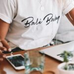 woman in white crew neck t-shirt sitting by the table with macbook